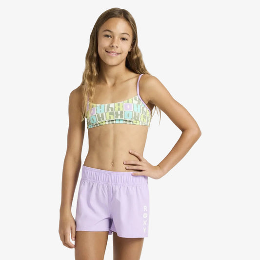 Young girl wearing a colorful bikini top and purple shorts on a white background