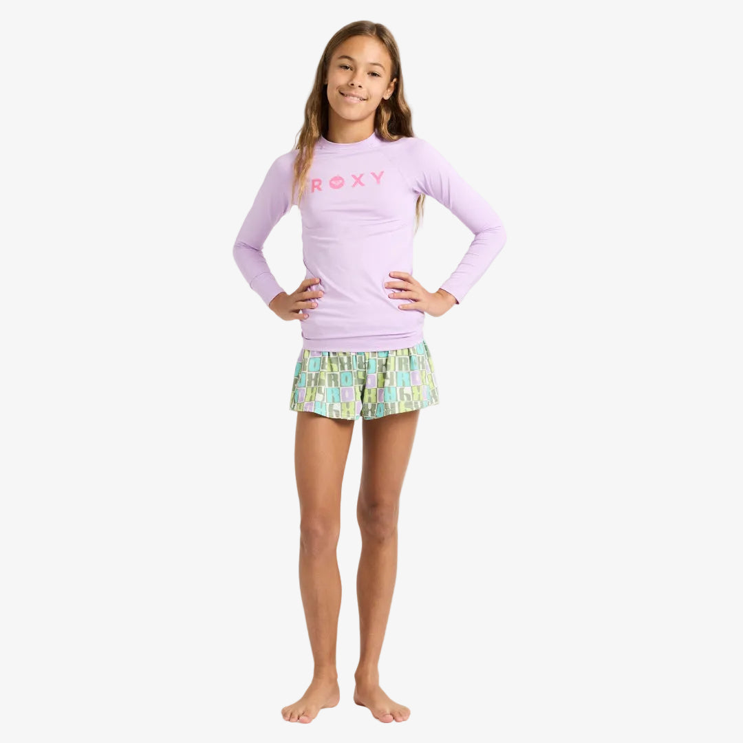 Young girl wearing a pink long-sleeve top and patterned shorts on a white background